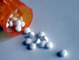 A closeup of some pills pouring out of a prescription bottle.