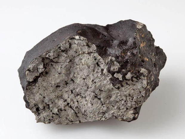 The 1.1 kg stone of the Tissint Martian meteorite at the Natural History Museum, London. The stone has a glossy black fusion crust. The fresh interior shows the large yellow/green olivine macrocrysts and pockets of black glass