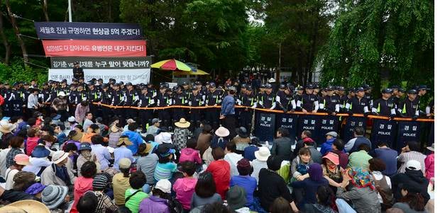 South Korean policemen stand guard in front of the main gate of the Evangelical Baptist Church premises, as church believers sit in front of the police barricade, in Anseong.