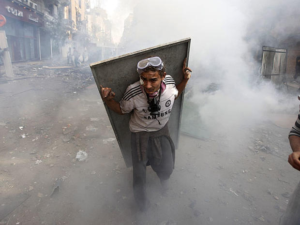 An Egyptian protester using scrap metal as a shield takes cover from tear gas during clashes with security forces near Tahrir Square in Cairo, Egypt, Nov. 23, 2011.