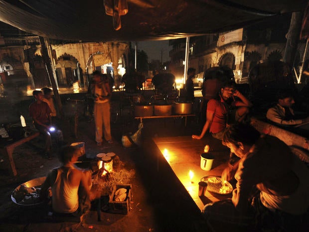 An Indian man prepares a meal as others sit at a roadside shop on a dark street following a power outage near a railway station in Allahabad, India, Tuesday, July 31, 2012.