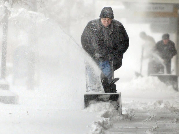 Chuck Carroll, center, uses a snowblower to clear the sidewalk in front of his business in downtown Salina, Kan., Feb. 21, 2013.