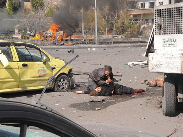 A man checks a woman's wrist for a pulse after a huge explosion in central Damascus