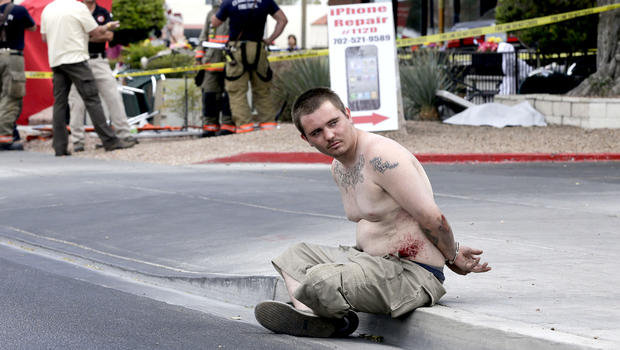A man sits handcuffed on the sidewalk waiting to be escorted away by police after crashing a vehicle into a crowded restaurant, Monday, April 1, 2013, in Las Vegas.