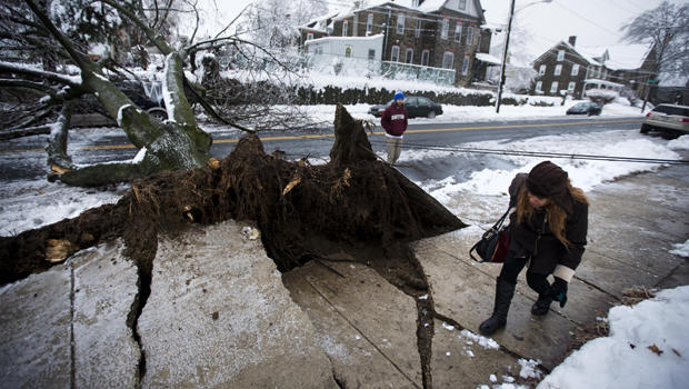 A woman ducks under a utility line next to an ice-covered downed tree that landed atop a minivan after a winter storm Feb. 5, 2014, in Philadelphia. 