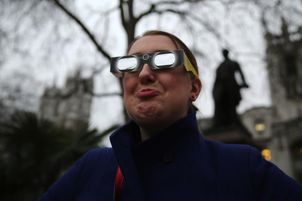A woman shows her disappointment while wearing protective glasses as she tries, unsuccessfully, to get a glimpse of the partial solar eclipse