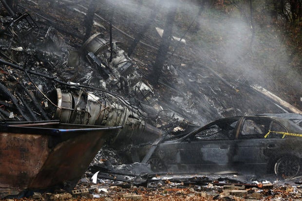 A charred car and aircraft debris smolder where authorities say a small business jet crashed into an apartment building in Akron, Ohio, Nov. 10, 2015.