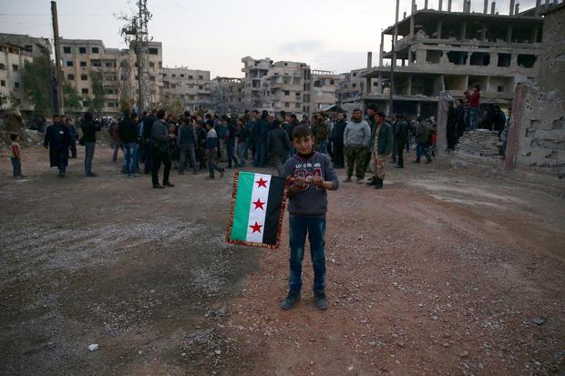 A boy carries an opposition flag as rebel fighters and civilians gather during the arrival of an aid convoy by the Syrian Arab Red Crescent and the United Nations to the rebel-held besieged town of Kafr Batna on the outskirts of Damascus, Syria, Feb. 23,