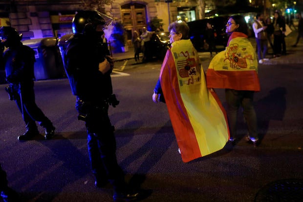Pro unity demonstrators wear Spanish flags as they walk past Catalan Regional Police officers during a protest after the Catalan regional parliament declared independence from Spain in Barcelona