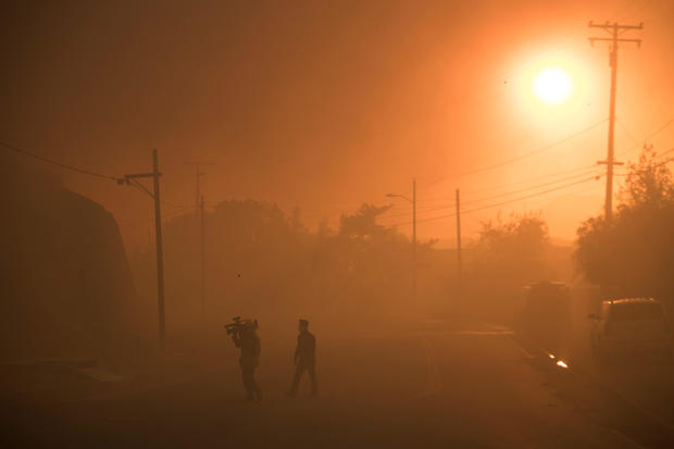 A TV crew walks through smoke as they work covering a wind driven wildfire in Ventura, California 