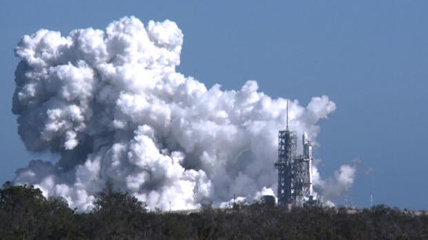 A towering exhaust plume billows into the afternoon sky during a test-firing of the 27 engines making up the three core-stage boosters in SpaceX's new Falcon Heavy rocket at the Kennedy Space Center in Florida on Jan. 24, 2018.