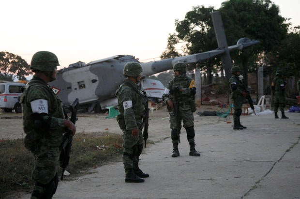 Soldiers stand guard next to a military helicopter, carrying Mexico's interior minister and the governor of the southern state of Oaxaca, crashed on top of two vans in an open field while trying to land in Santiago Jamiltepec