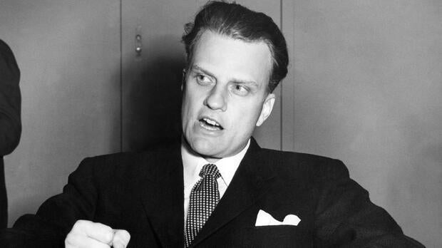 Billy Graham, the American evangelist, pounds his knee as he is interviewed aboard the SS United States on Feb. 26, 1954, upon his arrival in Southampton, England, from New York.