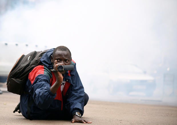 A Ugandan journalist uses his camera after riot policemen fired tear gas to disperse activists led by musician turned politician, Robert Kyagulanyi, during a demonstrating against new taxes including a levy on access to social media platforms in Kampala