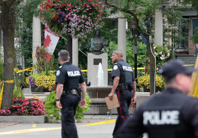 Police officers walk past Alexander the Great Parkette after a mass shooting in Toronto 