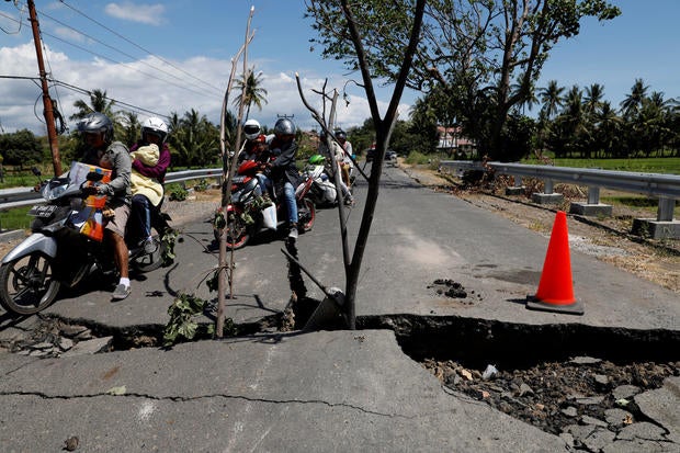 A family rides on a motorcycle through a crack on the street at Kayangan district after earthquake hit on Sunday in North Lombok