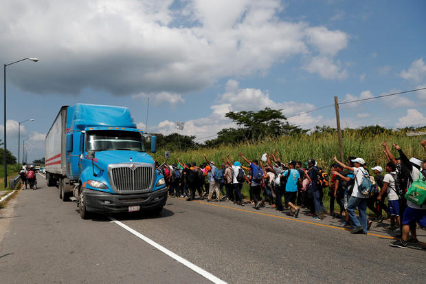Migrants, part of a caravan traveling from Central America en route to the United States, wave to a truck while walking by the road that links Ciudad Hidalgo with Tapachula 