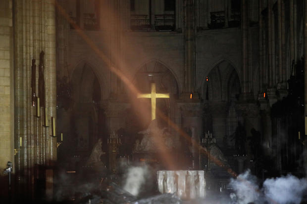 Smoke rises around the alter in front of the cross inside the Notre Dame Cathedral as a fire continues to burn in Paris 