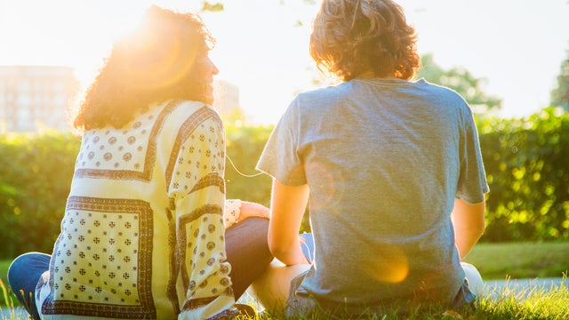 Rear view of mother sharing music sitting with teenager son 