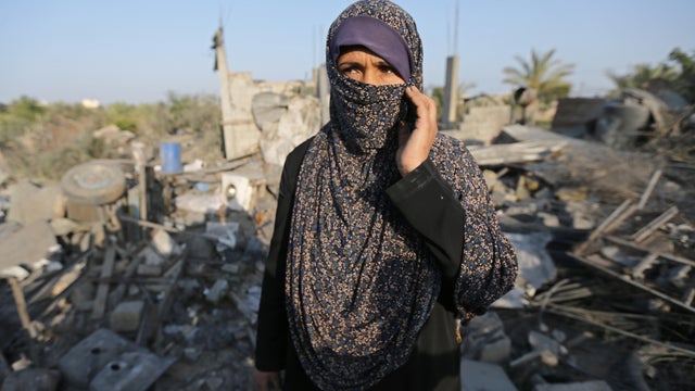 Palestinian woman looks on as she stands in front of a house destroyed in an Israeli air strike in the southern Gaza Strip