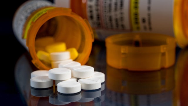 Macro of oxycodone opioid tablets with prescription bottles against dark background