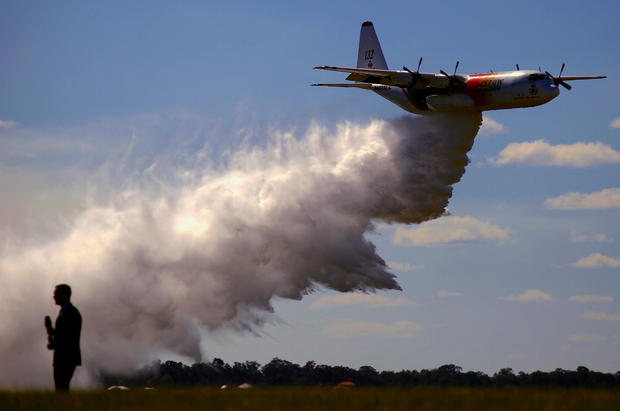 FILE PHOTO: A television reporter stands in front of the Large Air Tanker C-130 Hercules, also known as 'Thor', as it drops a load of around 15,000 litres during a display by the Rural Fire Service ahead of the bushfire season at RAAF Base Richmond in 