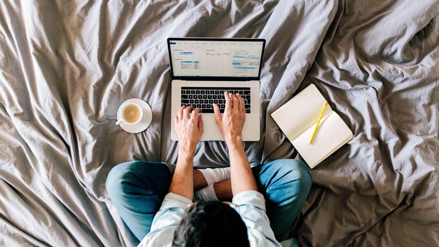 Overhead view of a man working on a laptop from his bed at home 