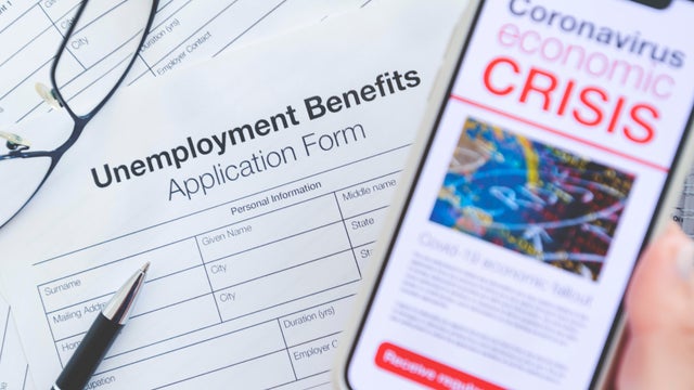 Close up of a mobile phone with Coronavirus covid-19 economic crisis news article. There is an unemployment benefits claim  form in the background on the desk 