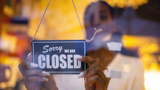 Woman putting closed sign on door of coffee shop 