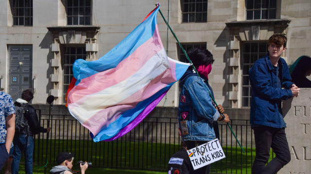 A protester holds a Trans Pride flag and a 'Protect Trans 